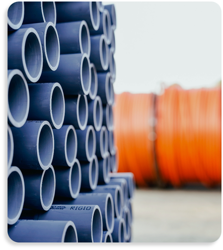 Stacked bundles of rigid grey PVC conduit and flexible orange HDPE pipes at OMNI warehouse