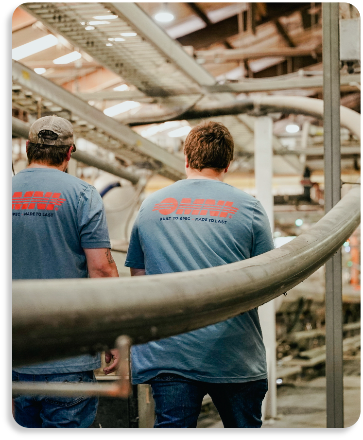 Two OMNI factory professionals standing on an elevated platform overseeing automated machinery conduits.