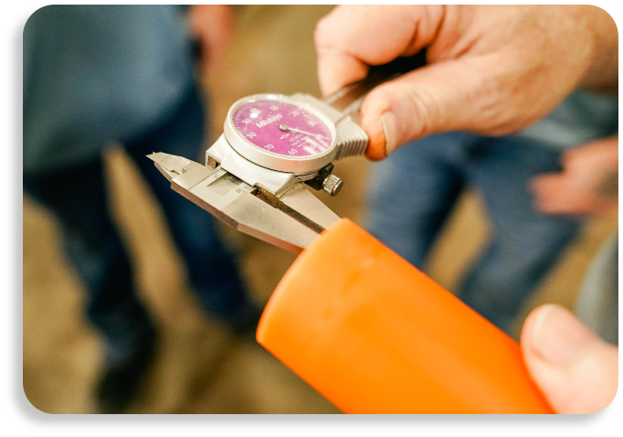 A close-up view of a quality inspector using a precision dial caliper gauge on an orange manufactured pipeline segment.