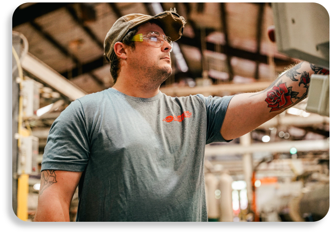 A plant professional in safety glasses looking upward on a busy infrastructure pipeline manufacturing floor