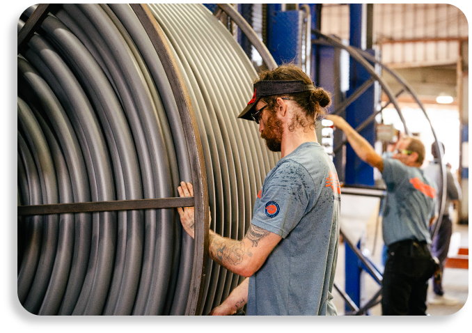 Two manufacturing specialists collaborating near a massive industrial reel winding high-quality conduit pipe.